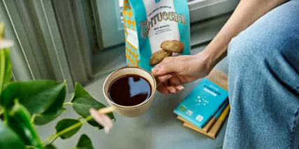 En hand som håller en kaffekopp bredvid ett paket kakor som Garant